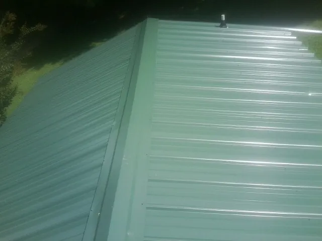 New green metal panels meeting at the ridge of a roof — Flat Roof Repair work by our crew in Palmyra